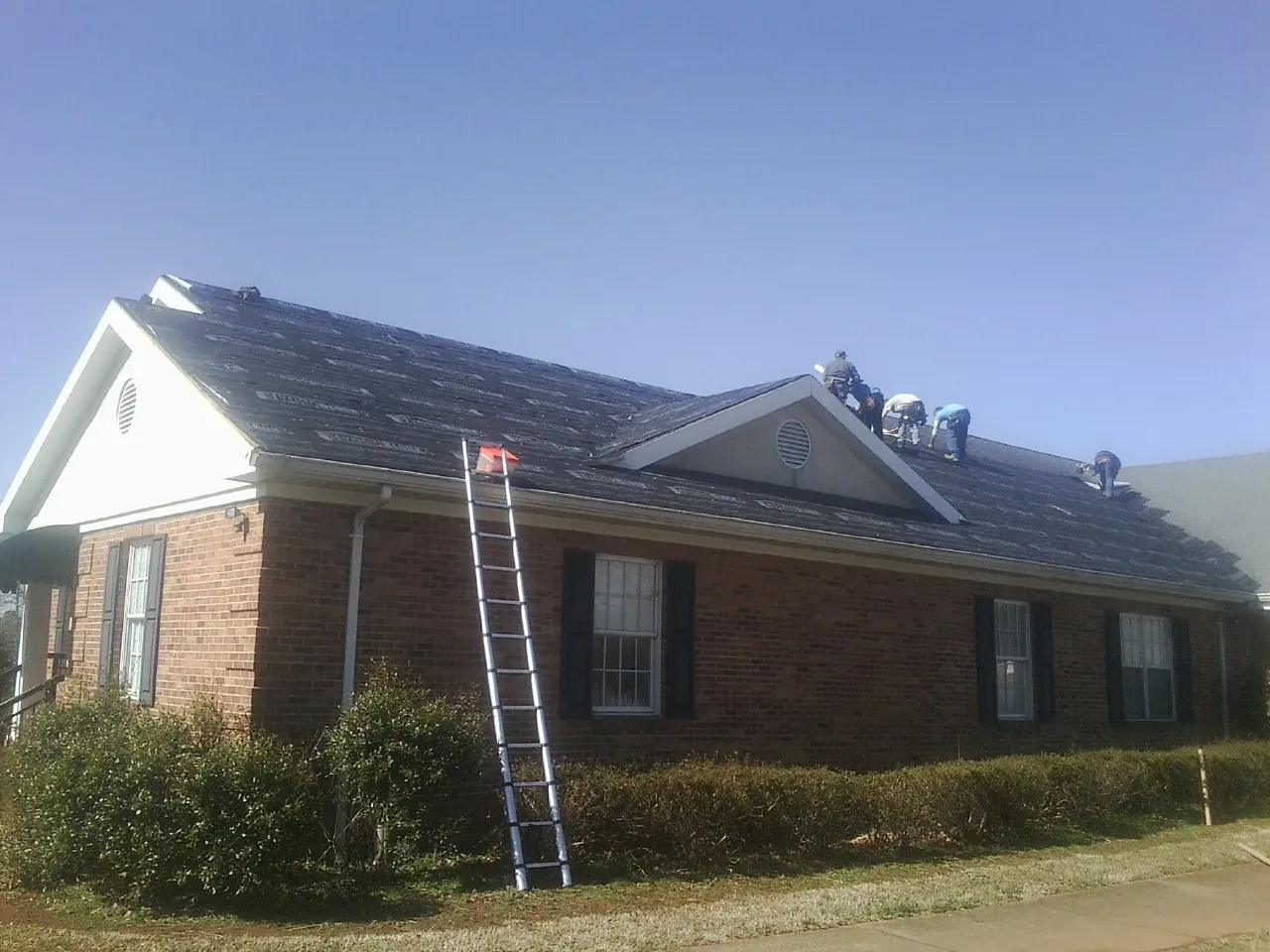 Crew tearing shingles off a brick ranch roof with a ladder set — Metal Roof Repair work by our crew in Womelsdorf