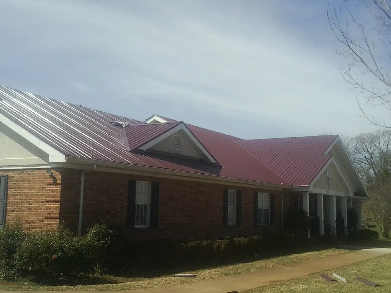 Red metal roof with gabled entries on a long brick building, from a Hail Damage Roof Repair job in Womelsdorf