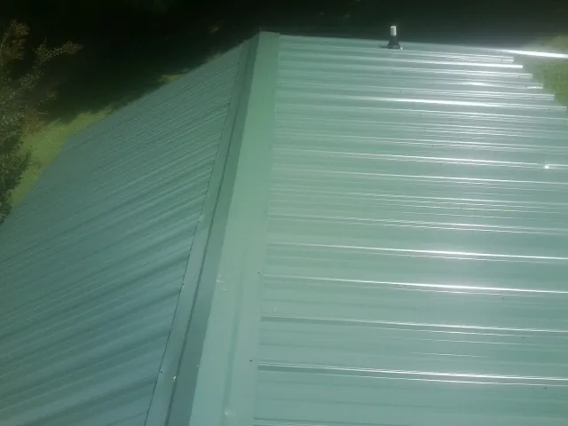 New green metal panels meeting at the ridge of a roof — Flat Roof Repair work by our crew in Womelsdorf