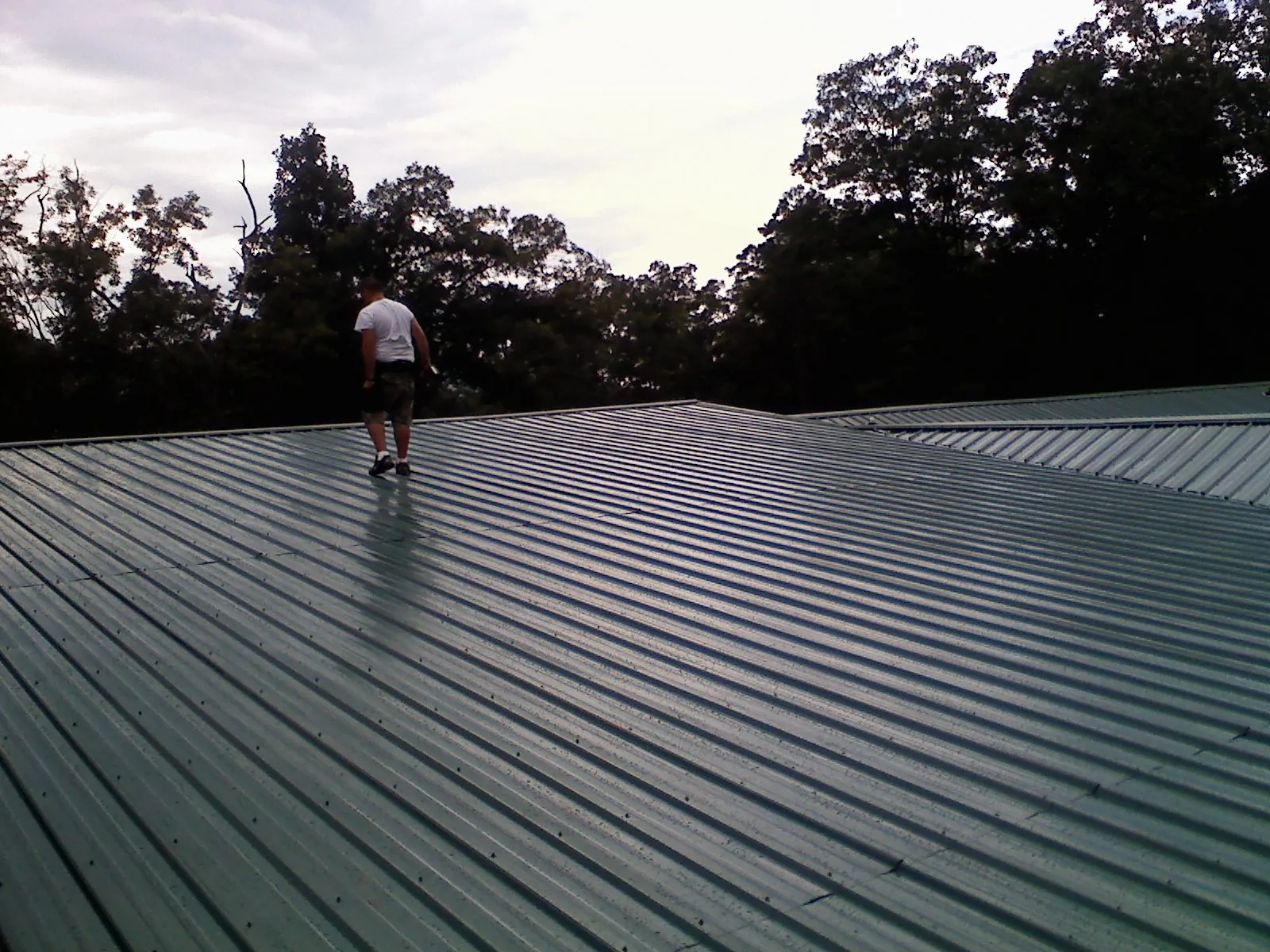 Roofer walking a wide expanse of new green metal roofing in Womelsdorf