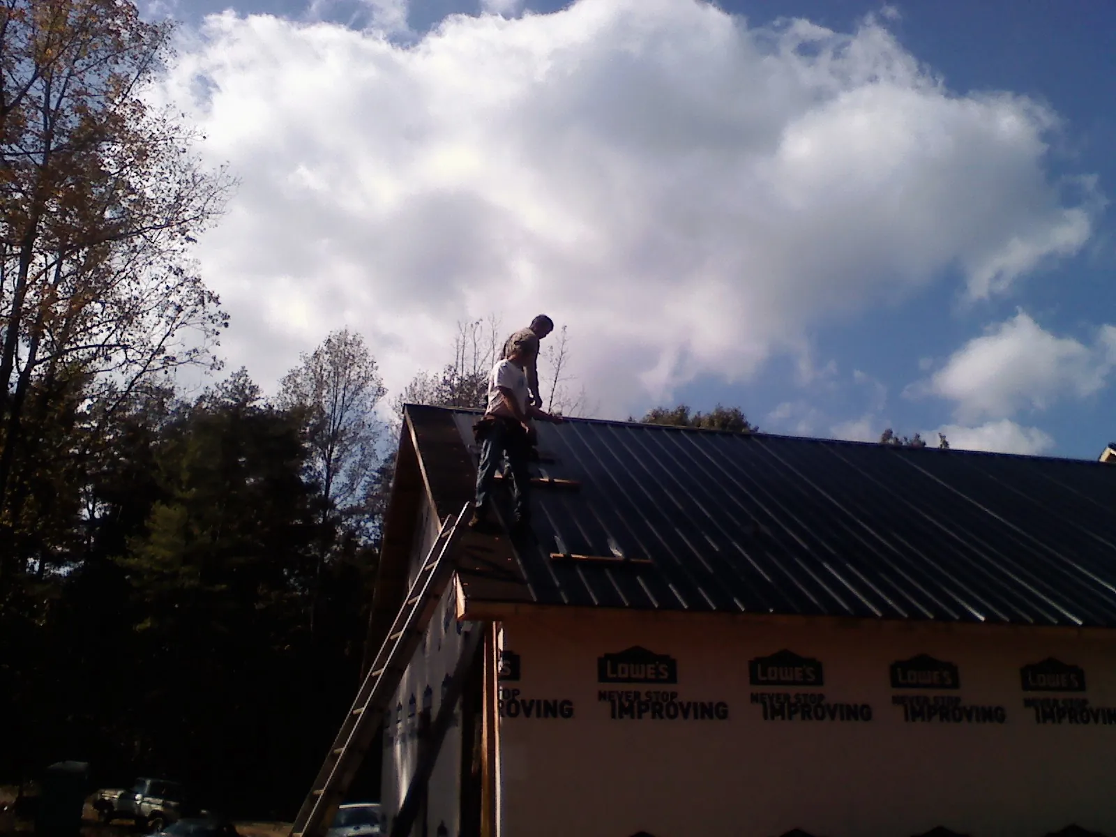 Roofer fastening dark metal panels high against a cloudy sky, from a Roof Inspection job in Womelsdorf