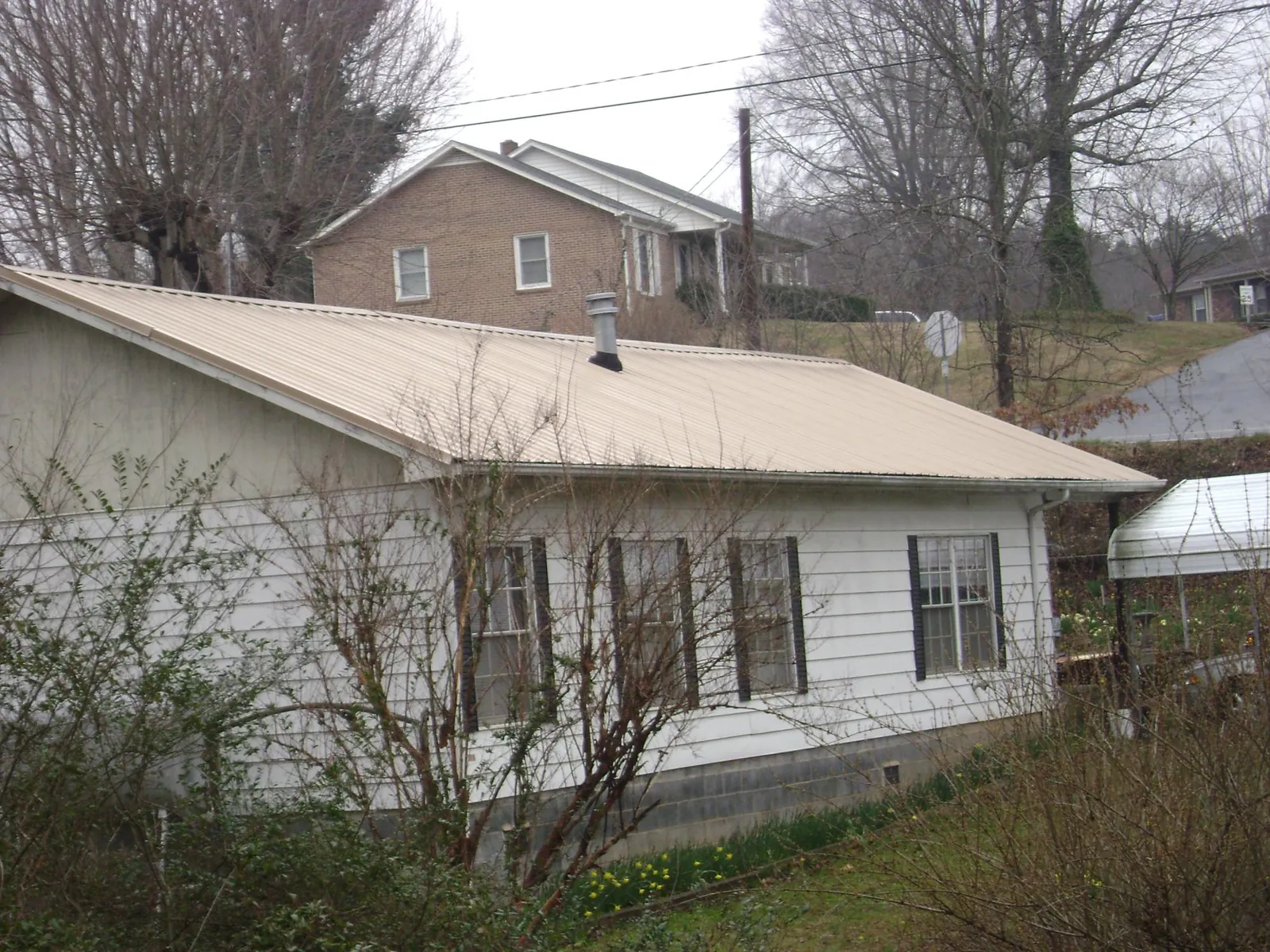 Tan metal roof on a white sided house set into a hillside — Commercial Roofing by Roofing Brothers in Womelsdorf